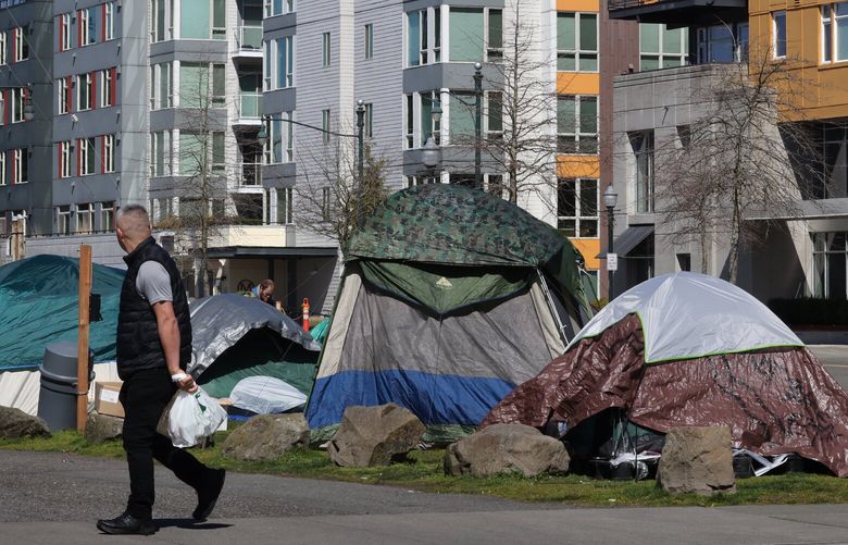 A man walks past a new homeless camp located at the corner of 6th Ave. SW and SW 152nd St. in Burien Tuesday, April 4, 2023.  After many homeless people who were living in tents outside of the Burien library were told they would have to be out by noontime on Friday, March 31, 2023, they picked up their tents and moved them a block away. More tents have been put up at the location and people in Burien are complaining.   223443
