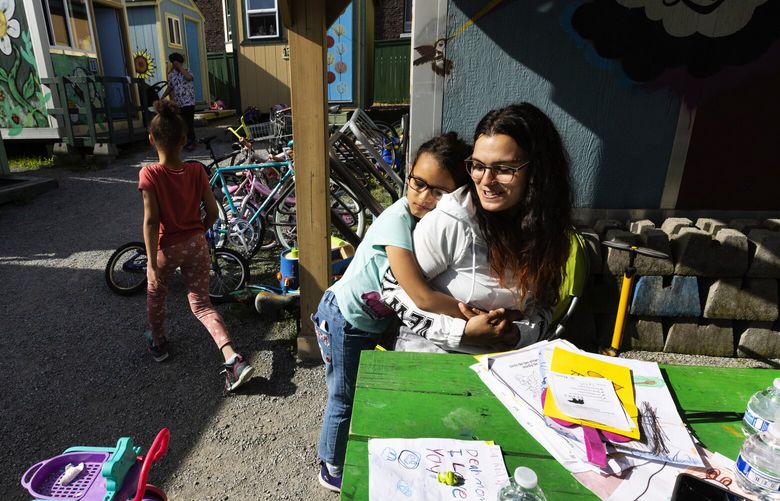 Selena Walley, 27, a mother who lives at a tiny house village in Seattle, gets a hug in the sun from her middle daugher, La’Riah, 6, as her oldest, Savannah, 8, goes to check out the bikes, Monday, May 8, 2023.