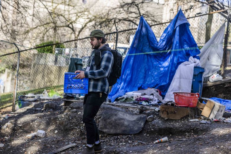 Daniel Godfrey, screening and outreach coordinator for the LEAD diversion program, hands out lunches and harm reduction supplies at a Seattle homeless encampment in February. (Daniel Kim / The Seattle Times)