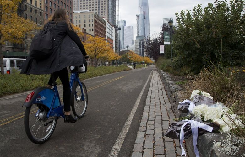 FILE – A bicyclist passes bouquets of flowers left by Argentine President Mauricio Macri and New York Mayor Bill de Blasio at the site of the terrorist attack on bicyclists, Nov. 6, 2017, in New York. Relatives of eight people killed in the Halloween terror attack on a New York City bike path, as well as those who were injured, are expected to speak at a Wednesday, May 17, 2023, sentencing hearing for an Islamic extremist who prosecutors say deserves multiple life sentences. (AP Photo/Mark Lennihan, File) NYSS212 NYSS212