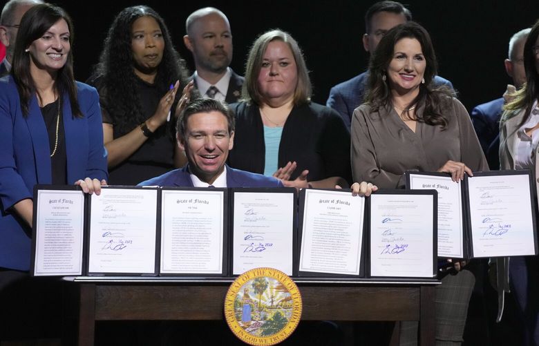 Florida Gov. Ron DeSantis holds up bills he signed during a bill signing ceremony at the Coastal Community Church at Lighthouse Point, Tuesday, May 16, 2023, in Lighthouse Point, Fla. (AP Photo/Wilfredo Lee) FLWL104 FLWL104