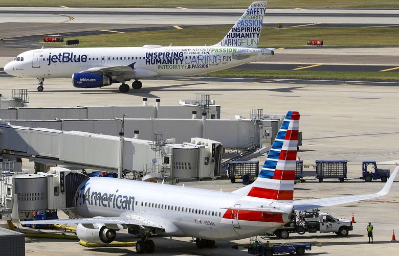 FILE – A JetBlue Airbus A320 taxis to a gate Wednesday, Oct. 26, 2016, after landing as an American Airlines jet is seen parked at its gate at Tampa International Airport in Tampa, Fla. The Justice Department is suing to stop American Airlines and JetBlue from coordinating their flights in the Northeast. Government antitrust lawyers said Tuesday, Sept. 21, 2021, that the deal between the two airlines will reduce competition and lead to higher fares. (AP Photo/Chris O’Meara, File) NYSB206