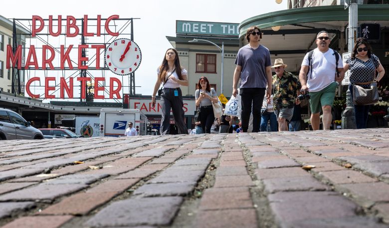 People cross the brick intersection at Pike Place Market on a sunny spring day. (Kevin Clark / The Seattle Times)