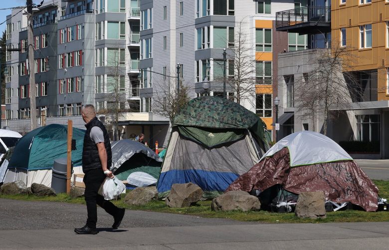 A man walks past a new homeless camp located at the corner of 6th Ave. SW and SW 152nd St. in Burien Tuesday, April 4, 2023. After many homeless people who were living in tents outside of the Burien library were told they would have to be out by noontime on Friday, March 31, 2023, they picked up their tents and moved them a block away. More tents have been put up at the location and people in Burien are complaining. 223443