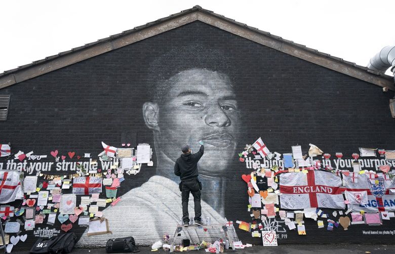 Street artist Akse P19 repairs the mural of Manchester United striker and England player Marcus Rashford on the wall of the Coffee House Cafe on Copson Street, in Withington, Manchester, England, on 2021. The mural was defaced with abusive graffiti in the wake of England losing the Euro 2020 soccer championship final match to Italy, but subsequently covered with messages of support by well wishers. (AP Photo/Jon Super, File)