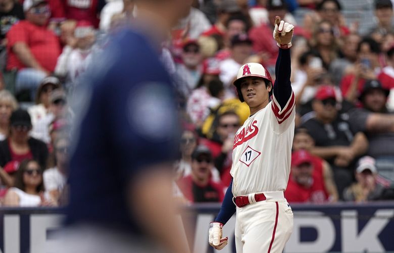 Los Angeles Angels’ Shohei Ohtani, right, gestures to Mike Trout as he stands on third after Trout singled during the third inning of a baseball game against the Seattle Mariners Sunday, June 11, 2023, in Anaheim, Calif. standing at left, is Mariners first baseman Ty France. (AP Photo/Mark J. Terrill) ANS113 ANS113