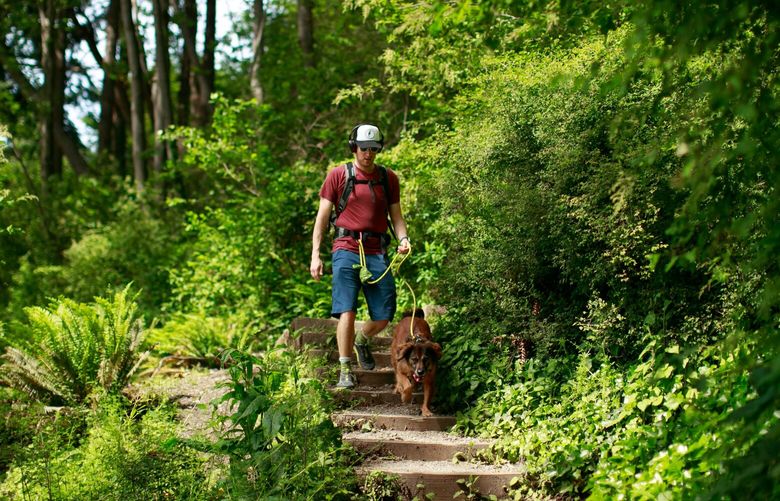 Evan Gwinn and his dog Dignan walk down a wooded trail down to the beach at Lincoln Park Wednesday, June 8, 2022. Gwinn says he was training to hike the Wonderland Trail. 
 220663