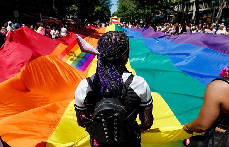 Laila James helps hold up a giant Pride flag as the Seattle Pride Parade makes it way down 4th Ave, Sunday, June 26, 2022 in Seattle, Wash. 220748