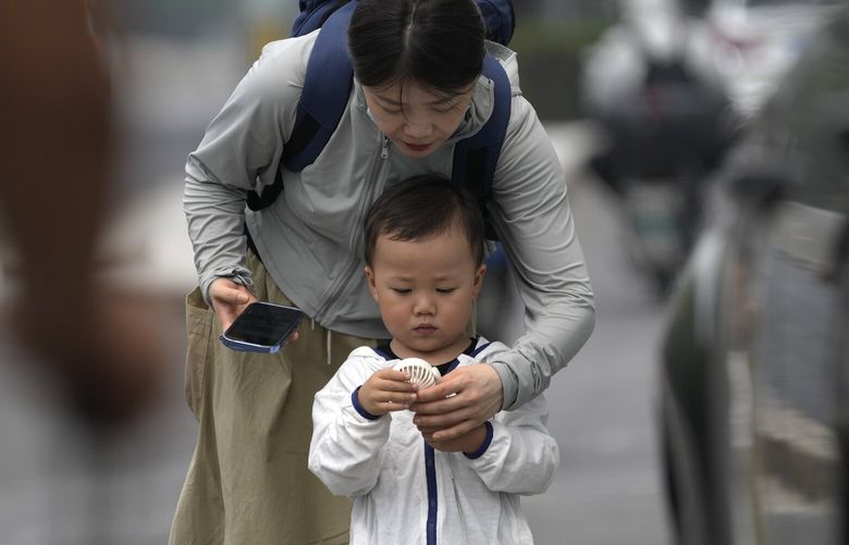 A woman helps a child to switch on an electric fan on a hot day in Beijing, Monday, July 3, 2023. Heavy flooding has displaced thousands of people around China as the capital had a brief respite from sweltering heat. Beijing reported 9.8 straight days when the temperature exceeded 35 C (95 F), the National Climate Center said Monday. (AP Photo/Andy Wong) XAW106 XAW106