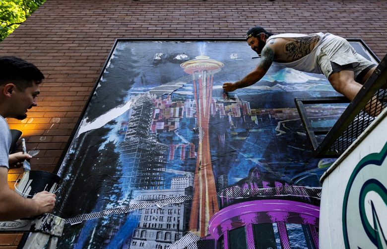 The artist A.Codd, left, is assisted by Chris Badley on Codd’s artwork for an exhibition of MLB-related murals in the RailSpur building alleyways, Monday, July 3, 2023 in Seattle’s Pioneer Square neighborhood.