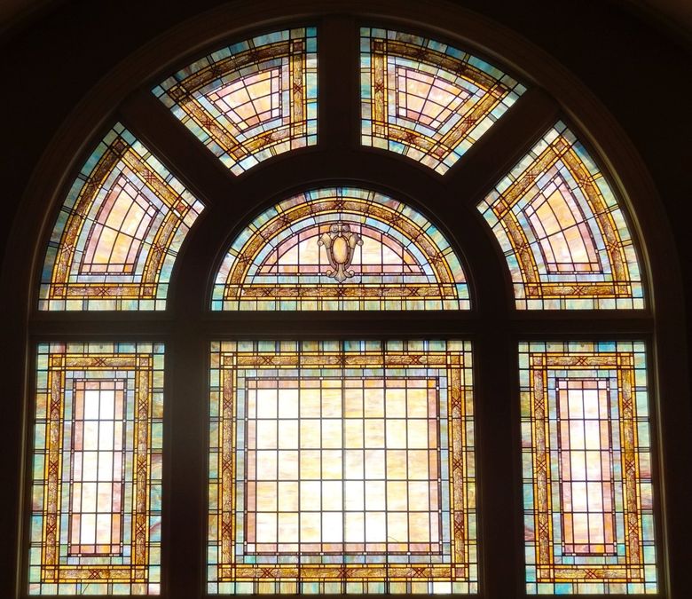 TOWN HALL SEATTLE: Large arched art glass windows are composed of painted and enameled glass acorn and leaf frames with a shield as the centerpiece of the arch. (Lawrence Kreisman)