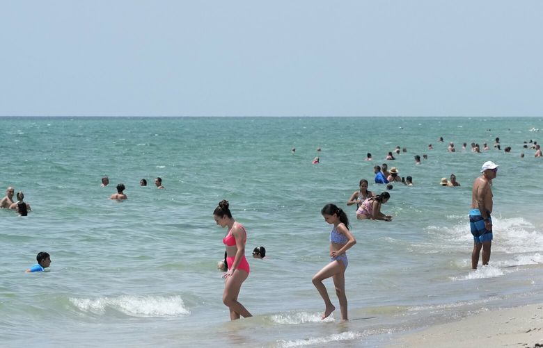 Beach goers take a dip in the Atlantic Ocean at Hollywood Beach, Monday, July 10, 2023, in Hollywood, Fla. Water temperatures in the mid-90s (mid-30s Celsius) are threatening delicate coral reefs, depriving swimmers of cooling dips and adding a bit more ick to the state’s already oppressive summer weather. (AP Photo/Wilfredo Lee) CLI101 CLI101