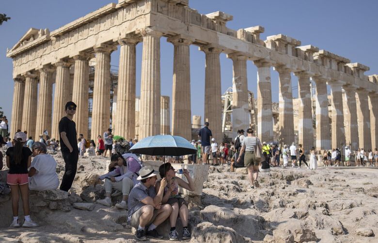 A tourist drinks water as she and a man sit under an umbrella in front of the five century BC Parthenon temple at the Acropolis hill during a heat wave, on Thursday, July 13, 2023. The government has announced emergency measures this week, allowing workers to stay home during peak temperature hours as a heat wave is due to affects most of Greece. (AP Photo/Petros Giannakouris) XPG101 XPG101