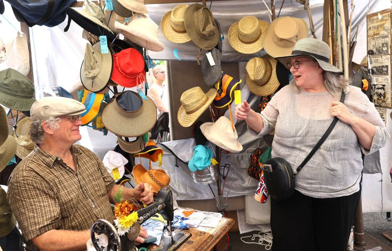 Emily Harris purchases a hat from Mike Leffler who owns the Hatterdashery at the West Seattle Summer Fest on a hot day when the temperatures hit almost 85 degrees in Seattle on Saturday, July 15, 2023.