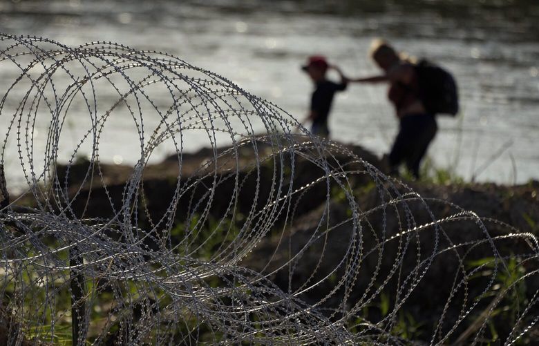 Migrants walk along concertina wire as they try to cross the Rio Grande at the Texas-U.S. border in Eagle Pass, Texas, Thursday, July 6, 2023. (AP Photo/Eric Gay) TXEG103 TXEG103