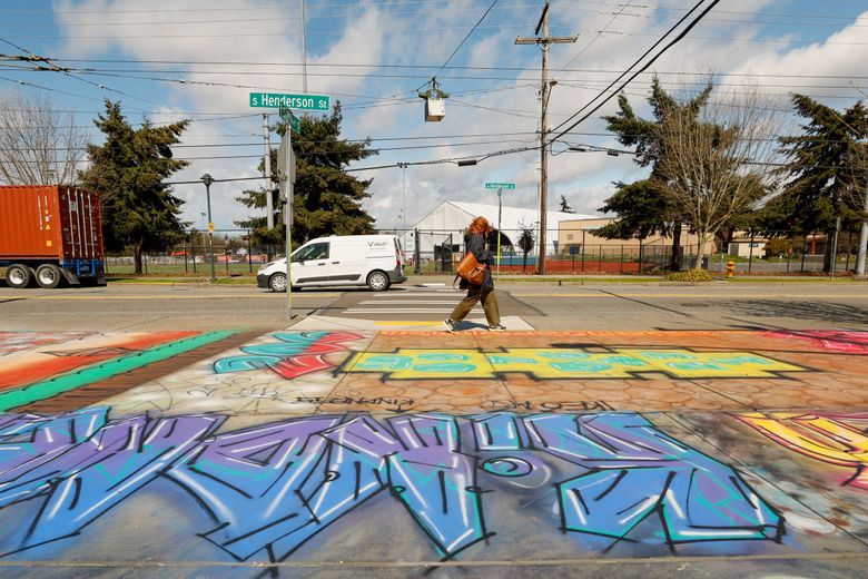 In April, a pedestrian crosses a street mural along South Henderson Street at the north side of the Mapes Walkway in Rainier Beach. (Jennifer Buchanan / The Seattle Times)