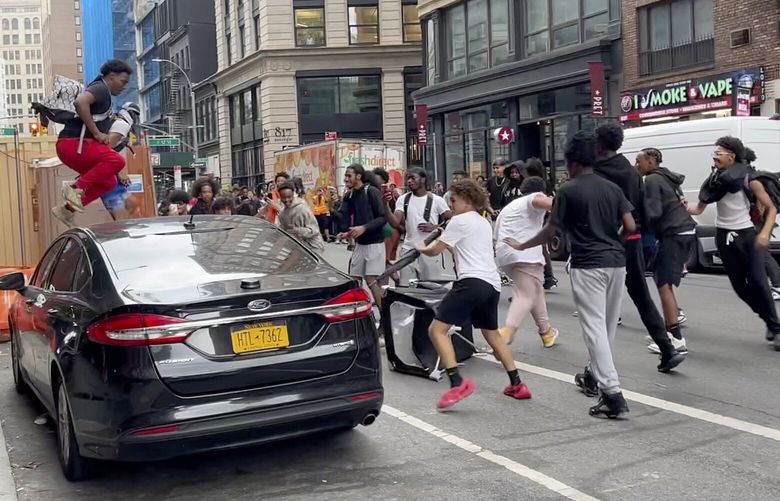In this photo taken from video, a man jumps on a car as a crowd runs through the street on Broadway near Union Square, Friday, Aug. 4, 2023, in New York. Police in New York City are struggling to control a crowd of thousands of people who gathered in Manhattan’s Union Square for an Internet personality’s videogame console giveaway that got out of hand. (AP Photo/Bobby Calvan) NYJJ101 NYJJ101