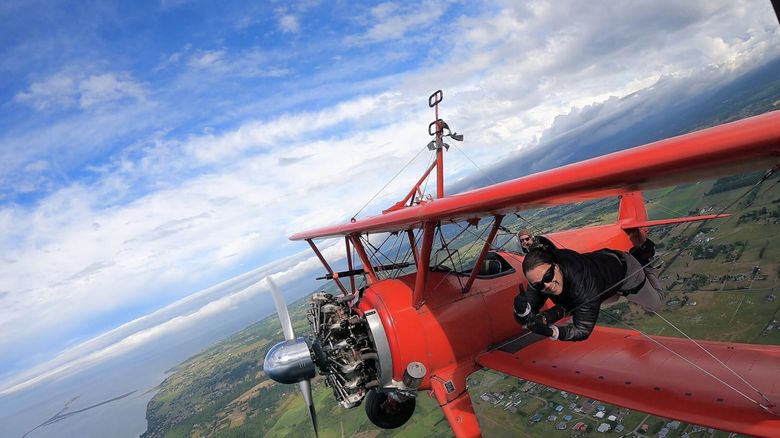 Jason Mayes lies astride a pole fastened to the cables between the upper and lower wings of a Stearman 450 biplane piloted by Mike Mason during a wing walking flight near Sequim in July 2021. (Courtesy of Mason Wing Walking)
