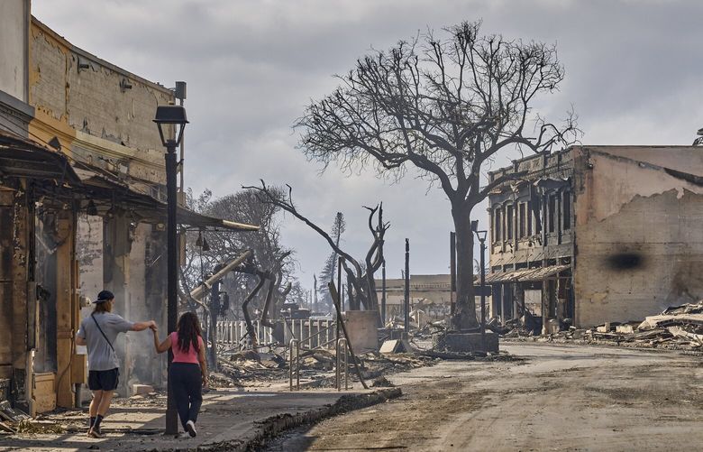 A couple walks past buildings destroyed by wildfires along Front Street in Lahaina, Maui, Hawaii, Aug. 10, 2023. Firefighters who rushed to contain the Maui wildfire found that hydrants were running dry, forcing crews to embark instead on a perilous rescue mission. (Philip Cheung/The New York Times) XNYT0381 XNYT0381