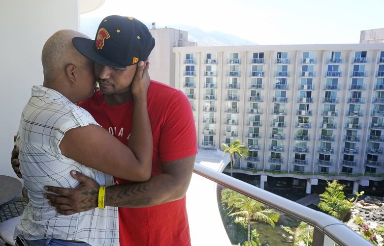 JP Mayoga, right, a chef at the Westin Maui, Kaanapali, and his wife, Makalea Ahhee, hug on their balcony at the hotel and resort, Sunday, Aug. 13, 2023, near Lahaina, Hawaii. About 200 employees are living there with their families. Officials urge tourists to avoid traveling to Maui as many hotels prepare to house evacuees and first responders on the island where a wildfire demolished a historic town and killed dozens of people. (AP Photo/Rick Bowmer) HIRB714 HIRB714