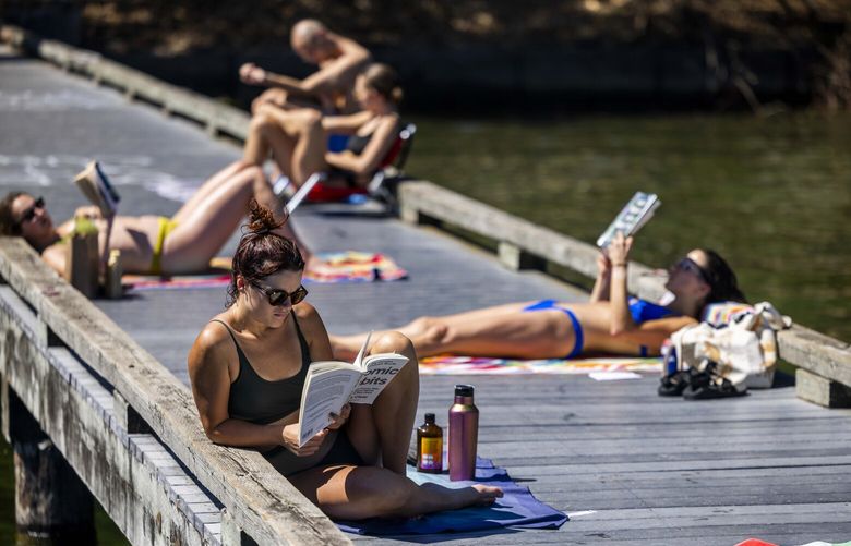 Taylor Pellizzari, center, sunbathes in the hot sun near Lake Washington with fellow book lovers on Aug. 16, 2023.