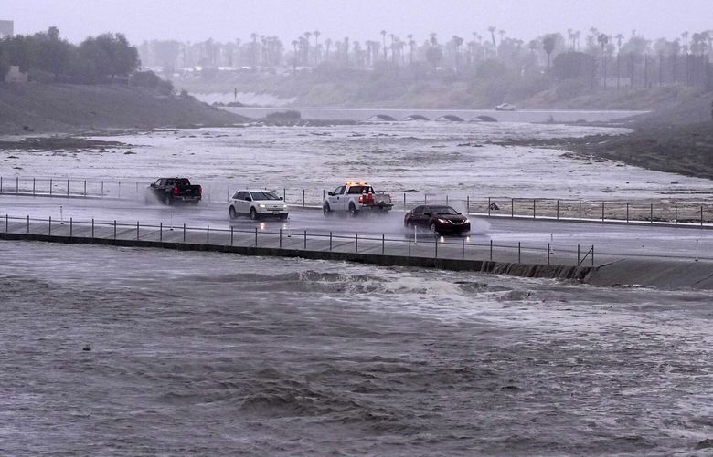 Vehicles cross over a flood control basin that has almost reached the street, Sunday, Aug. 20, 2023, in Palm Desert, Calif. Forecasters said Tropical Storm Hilary was the first tropical storm to hit Southern California in 84 years, bringing the potential for flash floods, mudslides, isolated tornadoes, high winds and power outages. (AP Photo/Mark J. Terrill) CAMT105 CAMT105