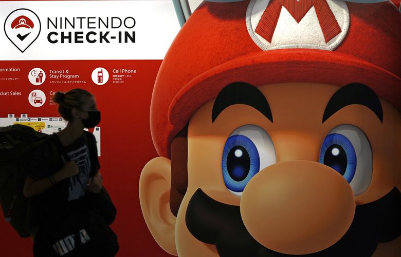 FILE – A person passes an ad featuring the Nintendo character Mario at Narita airport in Narita near Tokyo on June 10, 2022. Charles Martinet, the voice of Mario in Nintendo games since the 1990s, is stepping down, Nintendo of America confirmed Monday, Aug. 21. (AP Photo/Shuji Kajiyama, File) NYPM108 NYPM108