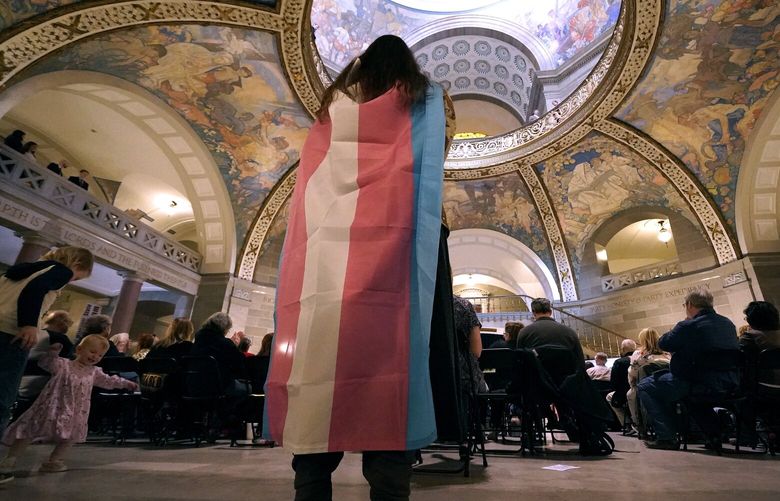 FILE – Glenda Starke wears a transgender flag as a counter protest during a rally in favor of a ban on gender-affirming health care legislation, March 20, 2023, at the Missouri Statehouse in Jefferson City, Mo. A Missouri judge said Friday, Aug. 25, that a law banning gender-affirming treatments for minors can take effect. St. Louis Circuit Judge Steven Ohmer ruled that the law will kick in Monday, Aug. 28, as previously scheduled. (AP Photo/Charlie Riedel, File) NYSS512 NYSS512