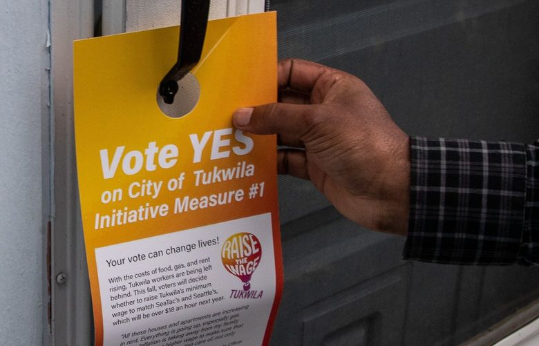 Motuma Debela leaves a Raise the Wage Tukwila door hanger on a home on 34th Place S on Friday, Oct. 21, 2022. The group is working to rally a large turnout of voters in support of a measure to raise Tukwila’s minimum wage.