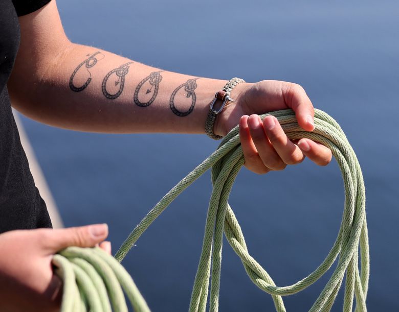 “I’ve always loved the bowline,” says Rose Vanasse, a lock and dam operator whose arm displays a “how to tie the knot in four steps&#8221; tattoo. Vanasse has worked at the Ballard Locks for 21/2  years and has a goal to become a lock master. She is holding a heaving line used to assist incoming boats with tying up. (Karen Ducey / The Seattle Times)