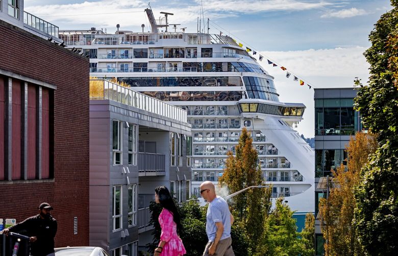 People cross Battery Street as Norwegian Encore cruise ship rises above Seattle buildings while docked at the Bell Street Cruise Terminal at Pier 66, Sunday, Sept. 10, 2023. According to the Port of Seattle’s 2023 cruise season webpage: “During the season stretching from April 15 to October 30, the Port forecasts that 289 sailings will carry 1.4 million revenue passengers, or 700,000 travelers, to Alaska and back.”
