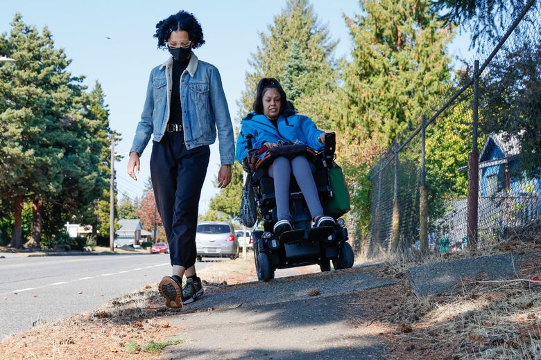 Tanisha Sepúlveda, right, and Amara Schermerhorn navigate an especially perilous stretch of sidewalk along 16th Avenue Southwest in West Seattle on Friday. Sepúlveda often rides her power wheelchair in the road because it has fewer obstacles but it can also be risky due to hostile or distracted drivers. Schermerhorn is legally blind and has a hard time seeing surface changes in the pavement. Both advocate for more and better-maintained sidewalks. (Jennifer Buchanan / The Seattle Times)