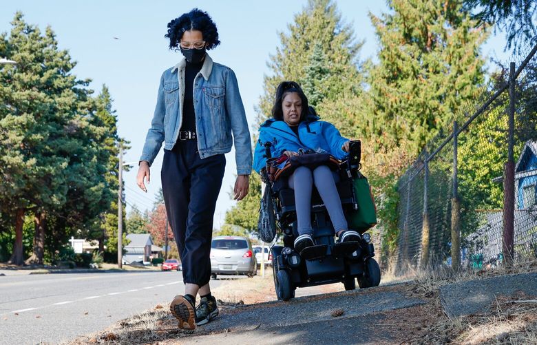 Tanisha Sepúlveda, right, and Amara Schermerhorn navigate an especially perilous stretch of sidewalk that has been pushed up by a large tree along 16th Ave SW Friday, Sept. 22, 2023 in West Seattle. Sepúlveda often opts to ride her power wheelchair in the street because it is smoother with fewer obstacles that could throw her from her chair but can also be equally perilous due to hostile or distracted drivers. Schermerhorn, who’s vision fluctuates throughout the day, is legally blind and has a hard time seeing surface changes in the pavement, especially when the sun sets. Both advocate for more and better-maintained sidewalks. 225027