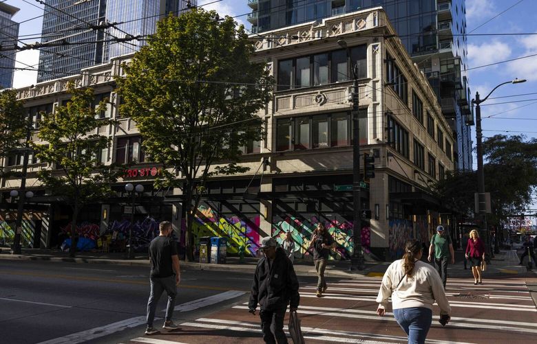 Community members walk past boarded up Kress building located at the intersection of 3rd Avenue and Pike Street in Seattle on Thursday, Sept. 21, 2023.