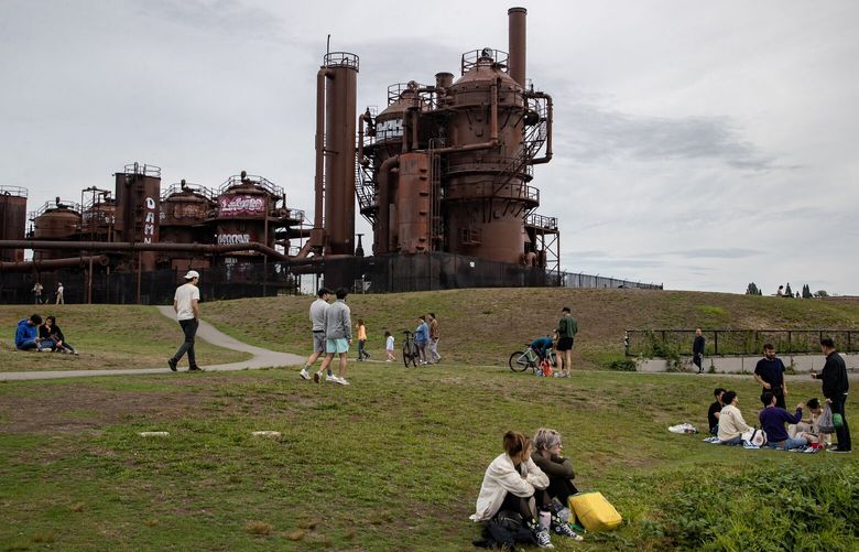 People lounge and walk under the looming metal structures at Gas Works Park. (Luke Johnson / The Seattle Times)