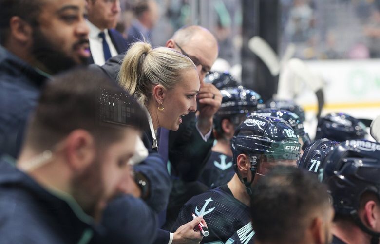 Jessica Campbell, center, assistant coach for the Coachella Valley Firebirds, works alongside Seattle Kraken coaches behind the bench during the second period of an NHL preseason hockey game against the Calgary Flames, Monday, Sept. 25, 2023, in Seattle. (AP Photo/Jason Redmond)