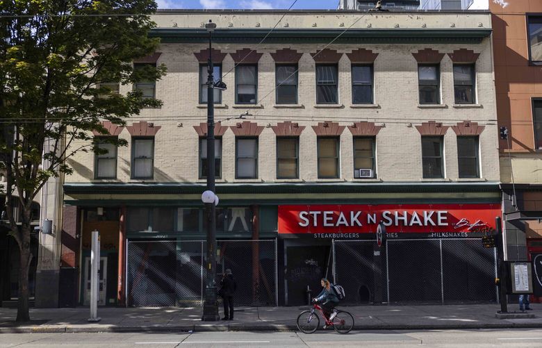 A bicyclist rides passes fenced off area near the now closed downtown location of the Steak N Shake on 3rd Avenue Seattle on Thursday, Sept. 21, 2023.