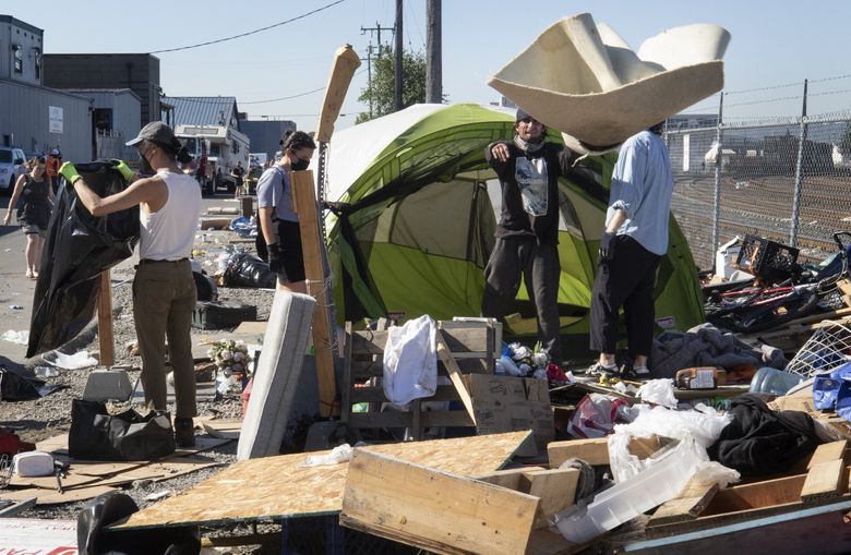 People pack up some belongings during a June 2022 sweep of the homeless camp on 3rd Avenue South in Seattle. In new court briefs, Seattle, San Francisco, Portland and other cities argue that their oft-stated goal of housing all the homeless is actually not possible. (Ellen M. Banner / The Seattle Times, 2022)