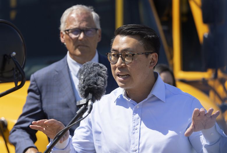 State Sen. Joe Nguyen, D-White Center, speaks to reporters at the Highline School District maintenance facility with Gov. Jay Inslee about high gas prices and oil company profits. Behind them are electric buses owned by the school district. (Ellen M. Banner / The Seattle Times)