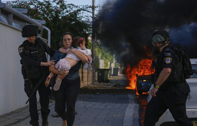 Police officers evacuate a woman and a child from a site hit by a rocket fired from the Gaza Strip, in Ashkelon, southern Israel, Saturday, Oct. 7, 2023. The rockets were fired as Hamas announced a new operation against Israel. (AP Photo/Tsafrir Abayov) XOB117 XOB117