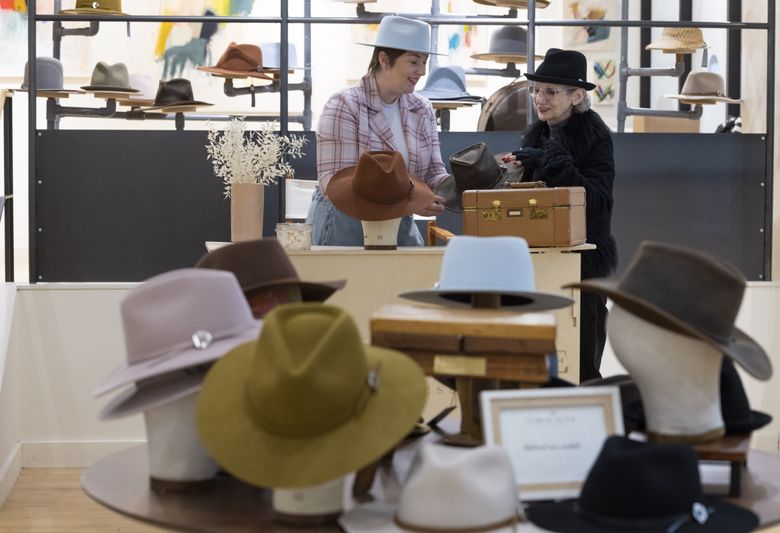 Jamie Slye, left, owner of Jamie Slye Hats + Accessories in downtown Seattle, chats about a hat with customer Lily Camarda at the store on Fifth Avenue in downtown Seattle. (Ellen M. Banner / The Seattle Times)