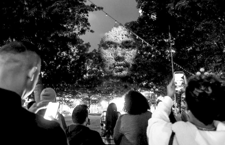 People at City Hall Park in Seattle take photos of the multimedia art installation MONUMENTS, which featured the faces and stories of Coast Salish tribes.