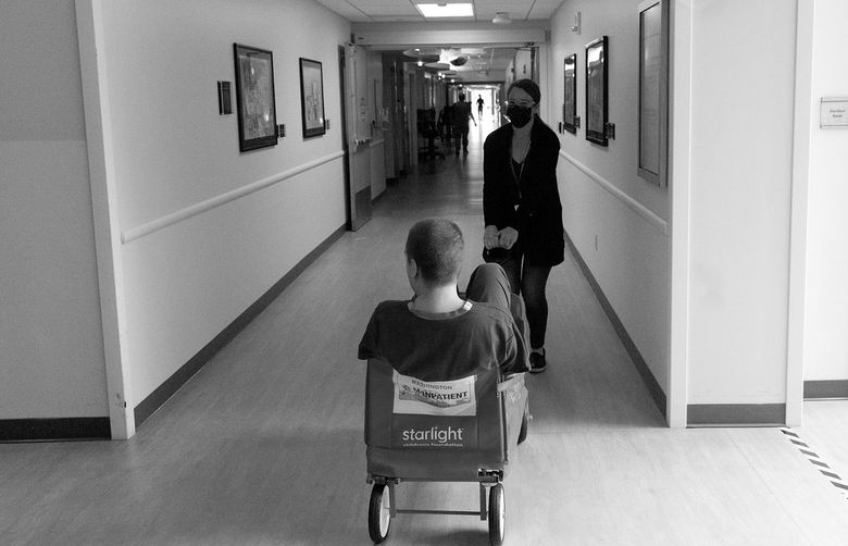 A teen patient gets a ride from his mom in a red wagon at Mary Bridge Children’s Hospital in Tacoma.