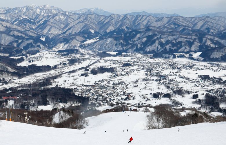 Skiers and snowboarders carve their way down a wide open run as they near the bottom of the Happo-One Snow Resort Feb 7, 2023 in Hakuba, Japan. The village of Hakuba can be seen in the valley.  ######