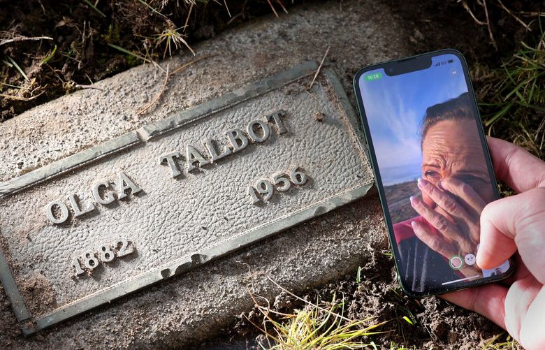 Alli Birrenkott, from Boulder City, Nevada, tears up while speaking with her son, Matthew over Facetime on his phone at the grave of his great-grandmother, Olga Talbot, at the Evergreen Washelli Memorial Park in Seattle on November 29, 2023. Matthew Birrenkott and his mother, Alli, previously were able to trace clues to the grave after The Seattle Times digitized previously unreleased records of Northern State admissions. Olga Talbot was institutionalized at Northern State Hospital for 30 years.