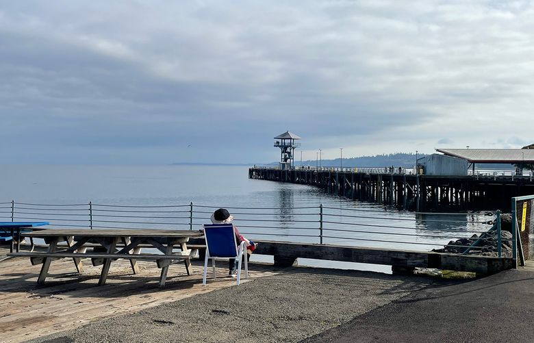 A person sits on a chair overlooking the water at a pier in Port Angeles