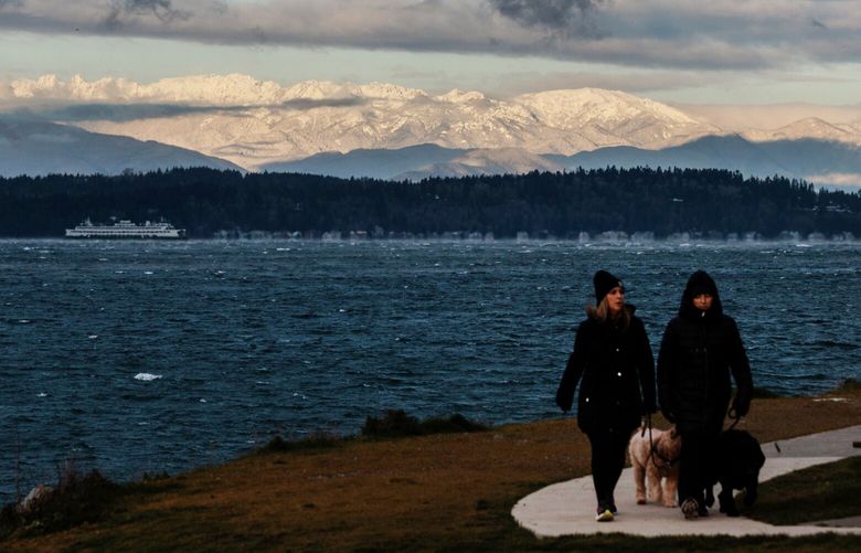 Bundled up pedestrians walk along Beach Drive SW as sun shines on the new snowfall on the Olympic Mountains Friday, Jan 12, 2024.  225953