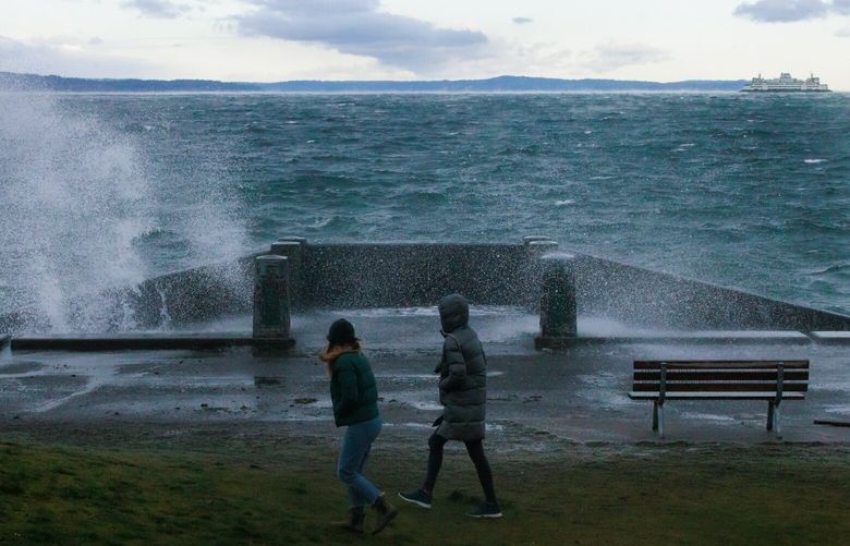 Bundled up pedestrians walk along a cold and windy Alki Beach as waves crash onto shore in Seattle Friday, Jan 12, 2024.  225953