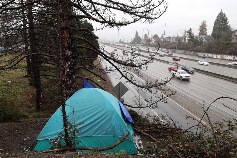 A tent is perched next to Interstate 5 as cars drive by on a rainy and cold Seattle afternoon. (Karen Ducey / The Seattle Times)