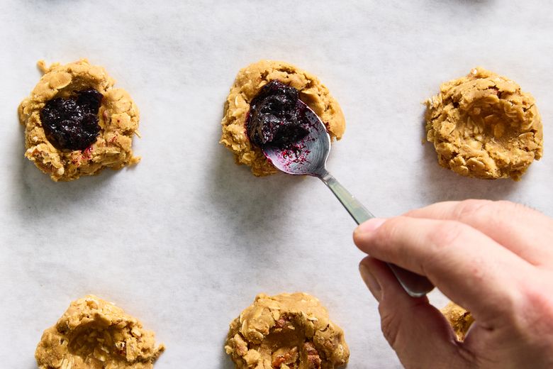 A dollop of blueberry jam fills a divot in the dough for each oatmeal cookie, in New York, Jan. 4, 2024. A puddle of blueberry maple jam is stuffed inside these tender, gently spiced treats. Food stylist: Barrett Washburne, prop stylist: Megan Hedgpeth (Ryan Liebe / The New York Times)